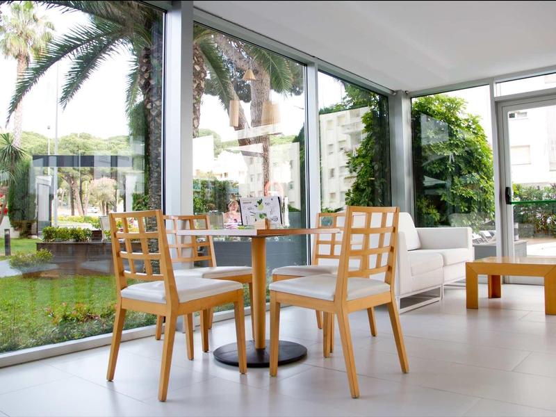 Espace moderne avec tables et chaises en bois à côté de grandes baies vitrées donnant sur un jardin.