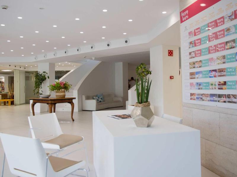 Hall d'hôtel moderne et lumineuse avec comptoir de réception, sièges et plantes.