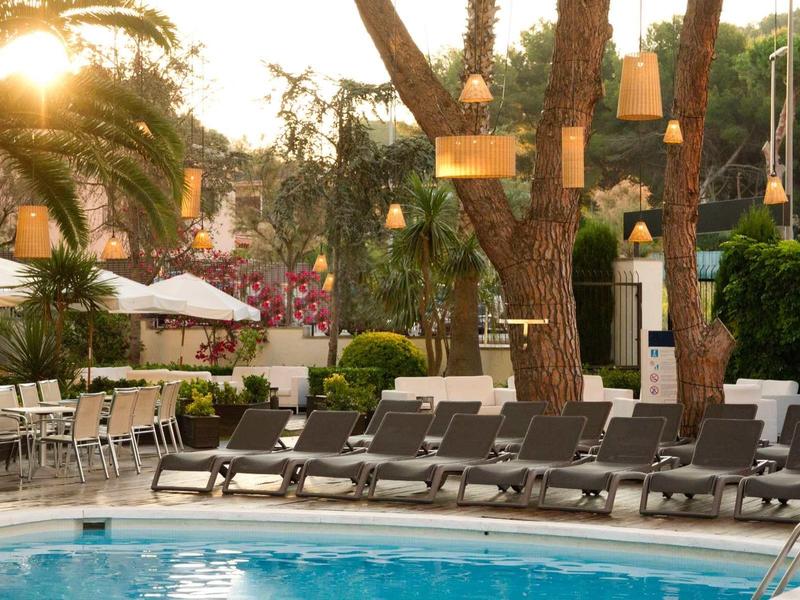 Coucher de soleil sur une piscine avec chaises longues et palmiers dans un jardin d'hôtel.