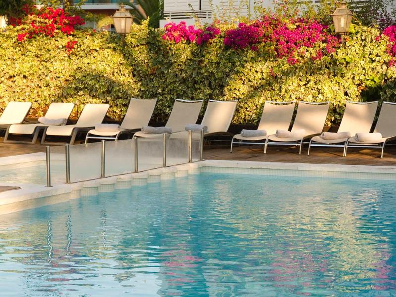 Une piscine accueillante avec des chaises longues devant des buissons fleuris au soleil.
