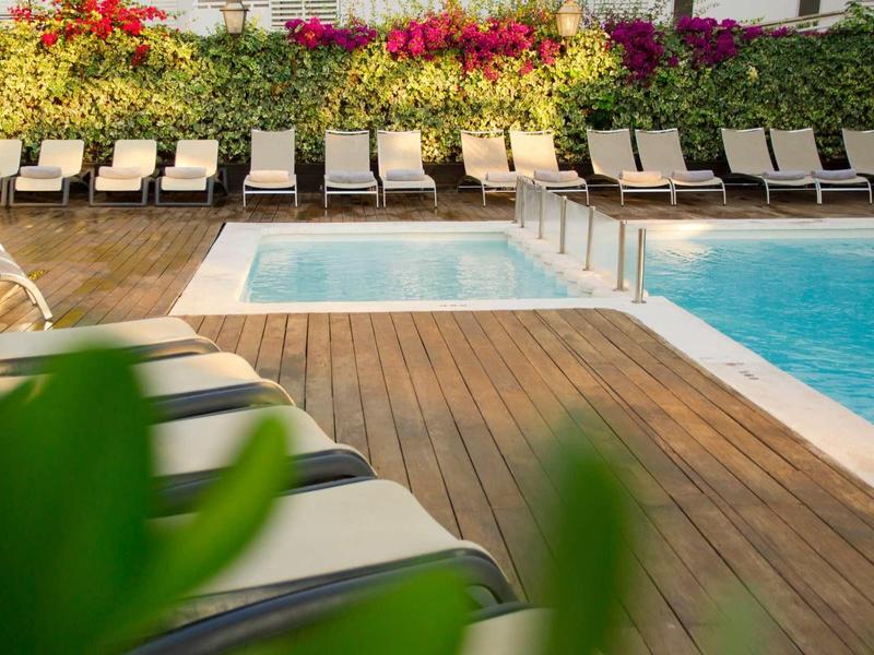 Piscine d'hôtel moderne avec terrasse en bois, chaises longues et fleurs colorées en arrière-plan