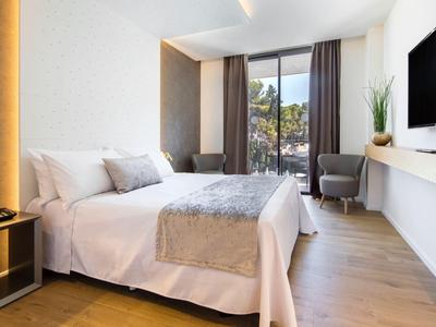 Nowoczesny pokój hotelowy z łóżkiem podwójnym, dużym oknem, krzesłem i telewizorem na ścianie.