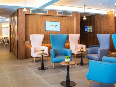 Przytulny kącik wypoczynkowy z kolorowymi fotelami i małymi stolikami w nowoczesnym wnętrzu hotelu.