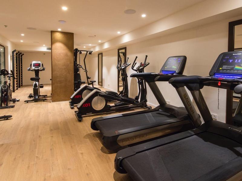 Nowoczesna siłownia hotelowa z bieżniami, trenażerami eliptycznymi i ciężarami w dobrze oświetlonym pomieszczeniu.