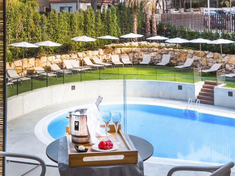 Strefa basenowa z leżakami i parasolami, na pierwszym planie taca z szampanem i owocami