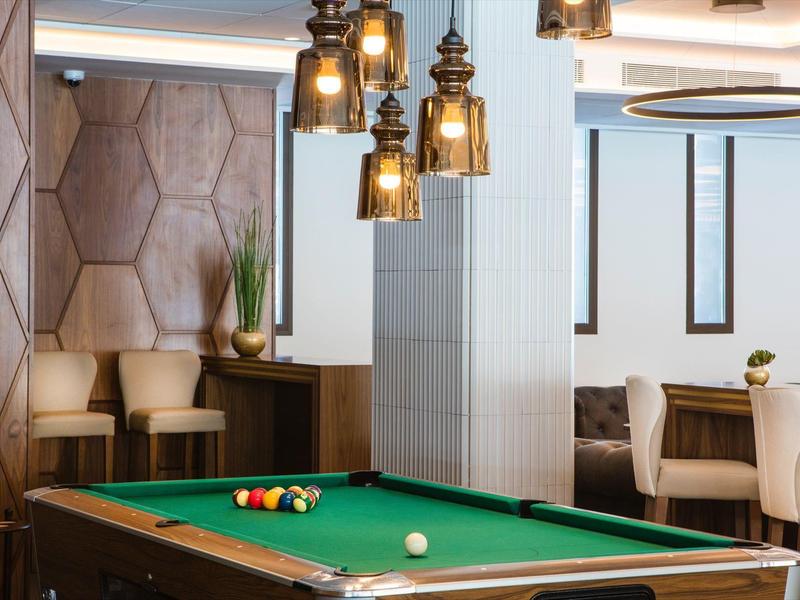 Nowoczesne pomieszczenie z bilardem, stylowymi lampami i przytulnymi miejscami do siedzenia w ciepłych tonach.
