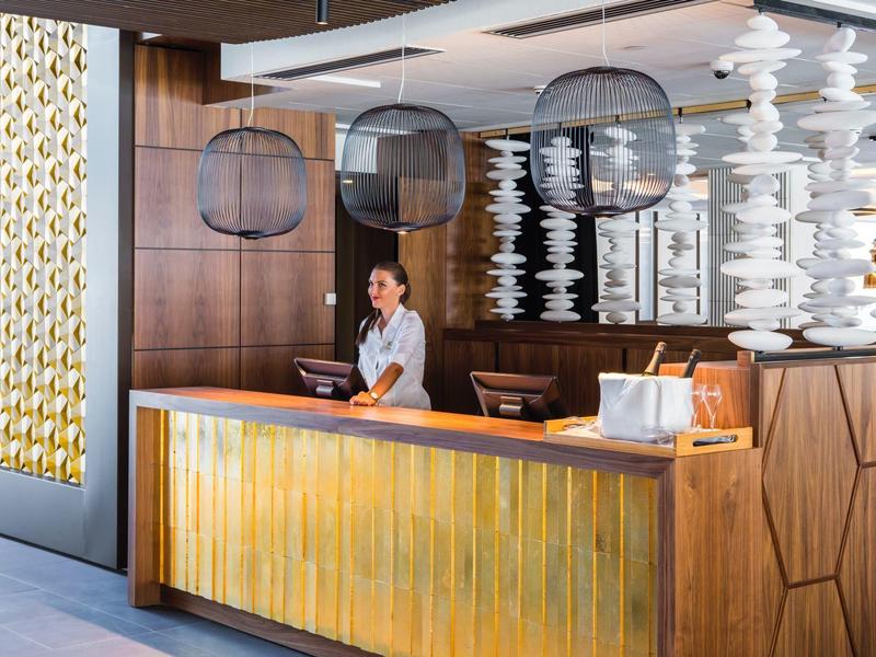 Nowoczesna lobby hotelowa z recepcjonistką za drewniano-mosiężnym biurkiem i stylowym oświetleniem.