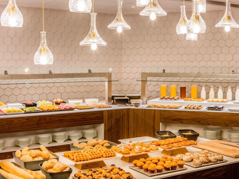 Bufet z różnymi wypiekami, sokami i owocami w jasnej restauracji hotelowej.