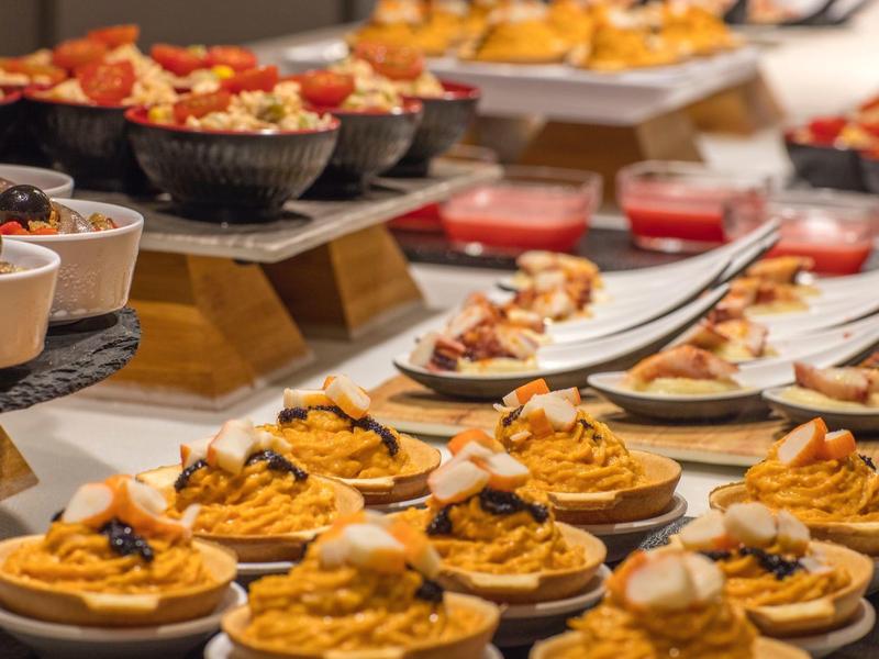 Bufet z różnymi małymi przekąskami i deserami ułożonymi na białych talerzach.