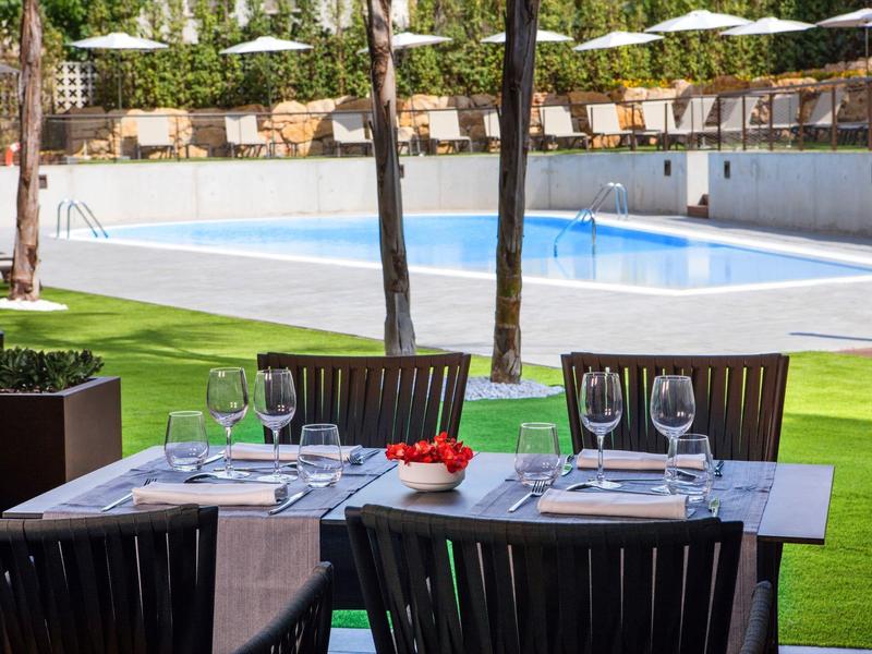 Elegancki zewnętrzny obszar jadalny z nakrytymi stołami obok basenu na zielonym trawniku.