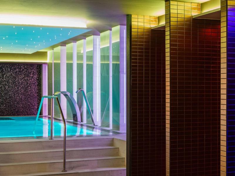 Nowoczesny basen kryty ze schodami, metalową poręczą i wielobarwnym oświetleniem.