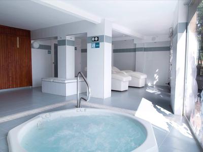 Jasna strefa wellness z jacuzzi i białymi fotelami obok dużych okien.