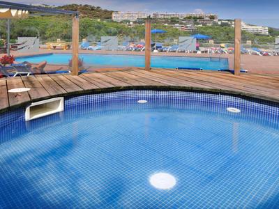 Piscine ronde avec terrasse en bois et terrains de tennis en arrière-plan.