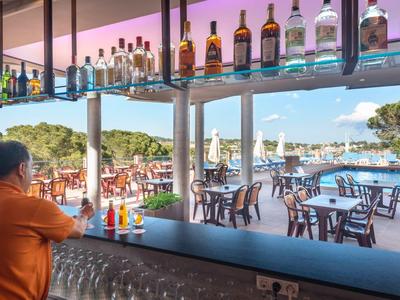 Widok z baru hotelowego na taras z stołami przy basenie i widokiem na morze.