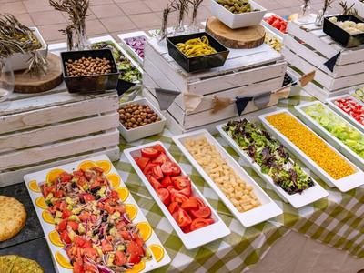 Bufet z różnymi sałatkami i potrawami w prostokątnych białych miskach na drewnianych skrzyniach.