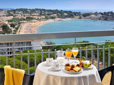 Stół na balkonie z śniadaniem i widokiem na morze nad ruchliwą piaszczystą plażą.