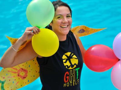Femme souriante tenant des ballons colorés près d'une piscine bleue.