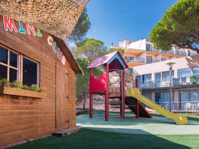 Plac zabaw dla dzieci ze zjeżdżalnią obok drewnianej chatki w ogrodzie hotelu.