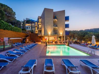 Nowoczesny basen hotelowy z leżakami i podświetlaną wodą o zachodzie słońca.