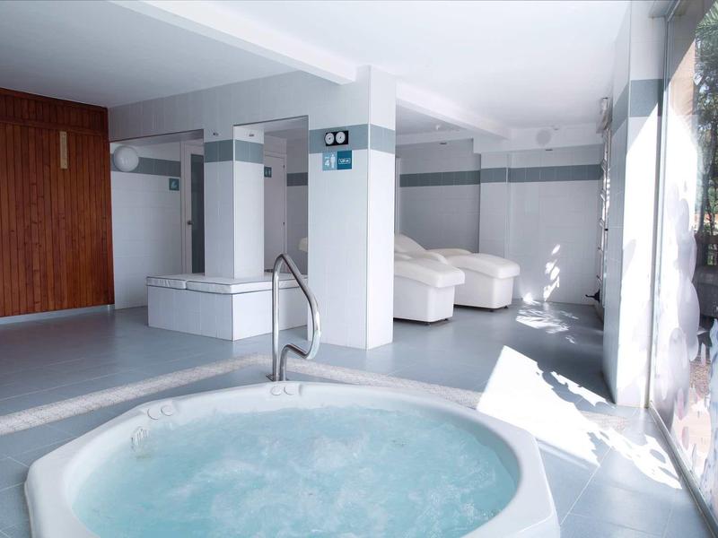 Jasna strefa wellness z jacuzzi i białymi fotelami obok dużych okien.