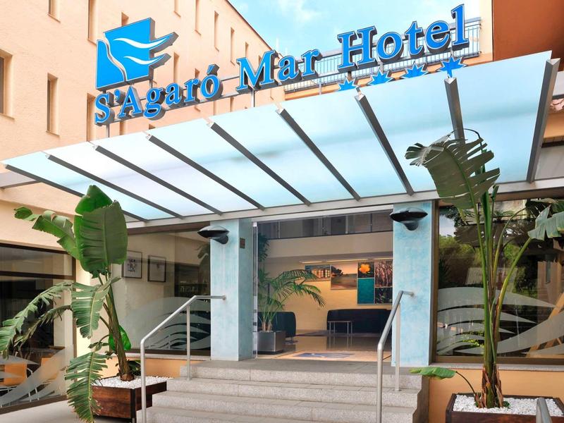 Wejście do hotelu St.Agáta Mar z niebieskim logo i nowoczesnymi szklanymi drzwiami pod daszkiem.