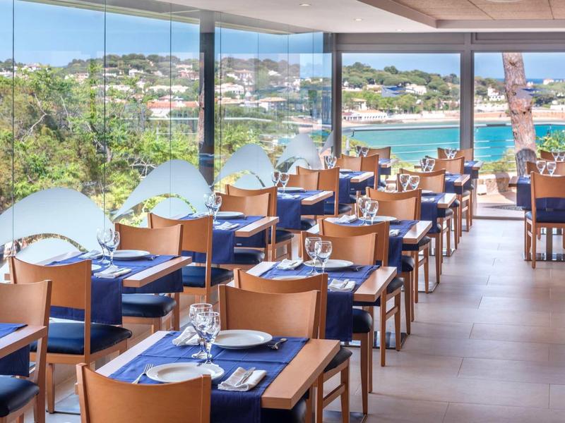 Nowoczesna restauracja z drewnianymi krzesłami i dużym panoramicznym oknem z widokiem na wybrzeże.