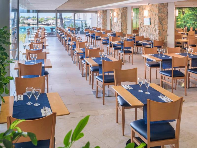 Nowoczesna restauracja z drewnianymi krzesłami i niebieskimi poduszkami, czysta i schludnie zaaranżowana.