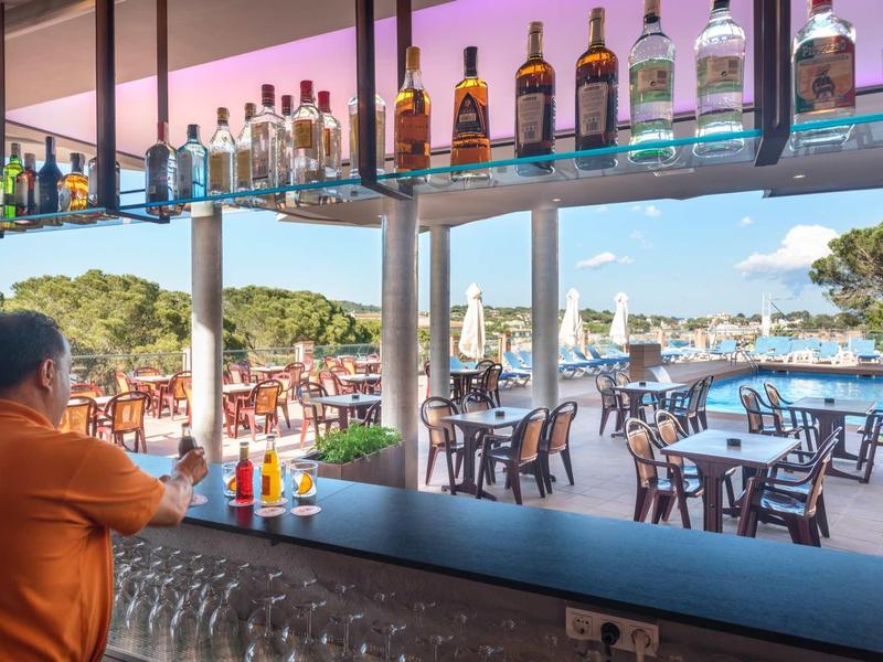 Widok z baru hotelowego na taras z stołami przy basenie i widokiem na morze.