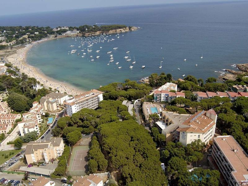 Widok z lotu ptaka na obszar nadmorski z piaszczystą plażą, wodą oraz wieloma budynkami i drzewami.