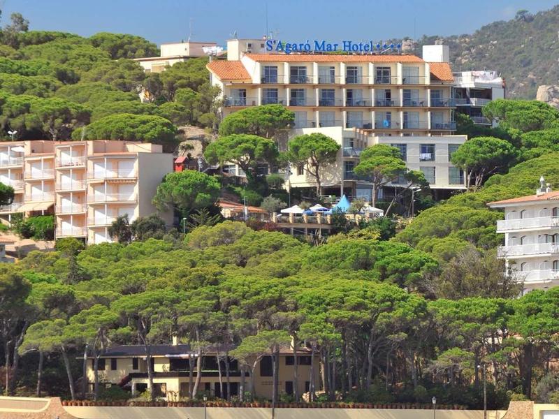 Hotel nad zalesionym wybrzeżem z widokiem na morze i żaglówką na pierwszym planie