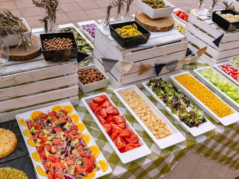 Bufet z różnymi sałatkami i potrawami w prostokątnych białych miskach na drewnianych skrzyniach.