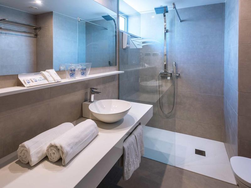 Nowoczesna łazienka z szklaną kabiną prysznicową, umywalką i ręcznikami na białej półce.