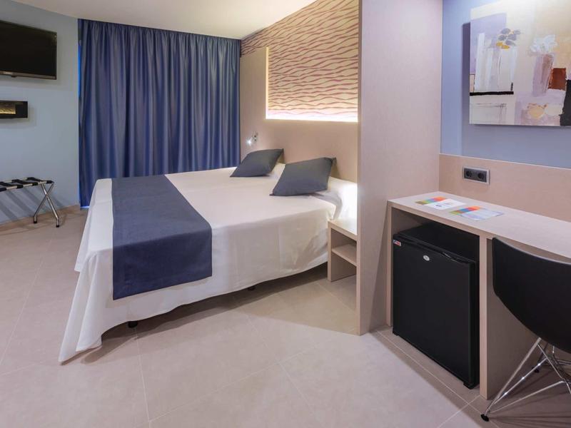 Nowoczesny pokój hotelowy z łóżkiem podwójnym, biurkiem, mini lodówką i dostępem do balkonu.