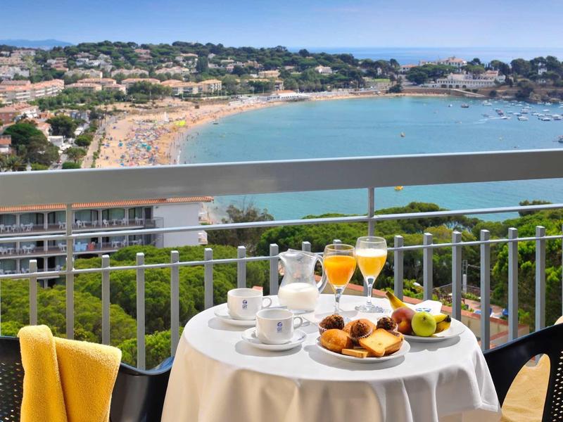 Stół na balkonie z śniadaniem i widokiem na morze nad ruchliwą piaszczystą plażą.