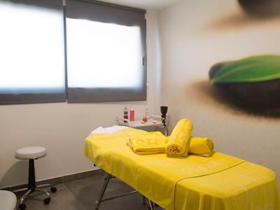 Salle de traitement avec table jaune, serviettes et tabouret près d'une fenêtre éclairée.