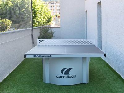 Moderner Tischtennistisch steht auf grünem Kunstrasen in einem engen Außenbereich.