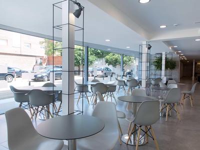 Café moderne avec chaises et tables blanches devant de grandes fenêtres donnant sur la rue.