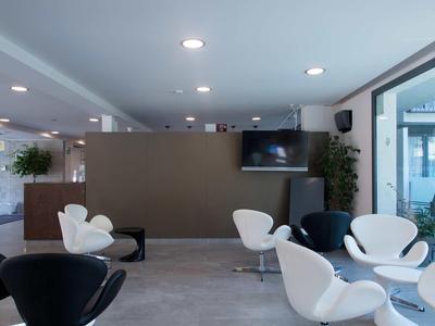 Espace lounge moderne d'hôtel avec des fauteuils blancs et noirs dans une pièce lumineuse.