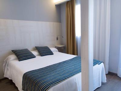 Chambre lumineuse avec un lit double et des oreillers et une couverture rayés bleus.