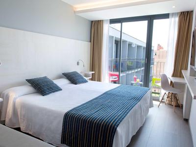 Chambre d'hôtel moderne avec lit double, literie bleue et blanche, et balcon avec coin salon.