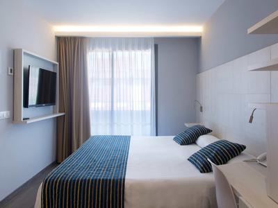 Chambre d'hôtel moderne avec lit double, deux oreillers et grande fenêtre avec rideaux.