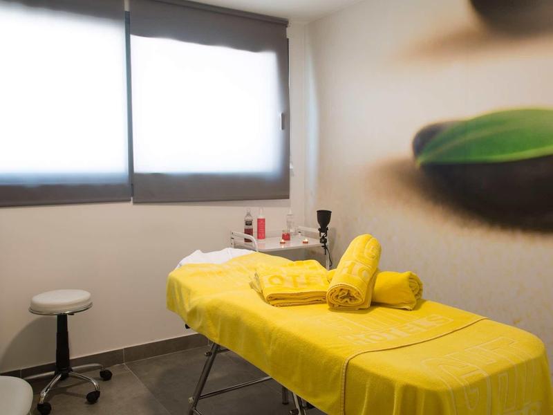 Salle de traitement avec table jaune, serviettes et tabouret près d'une fenêtre éclairée.