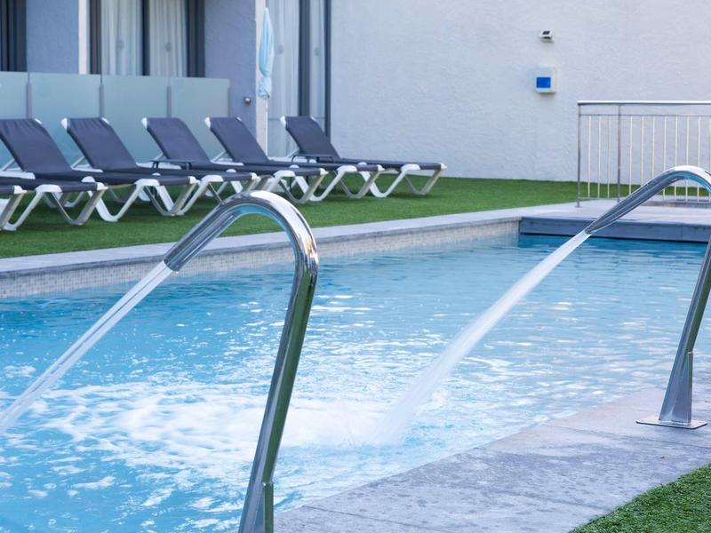 Piscine extérieure moderne avec chaises longues et jets d'eau à l'hôtel