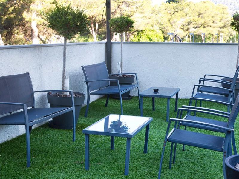 Espace extérieur moderne avec chaises bleues et tables sur gazon synthétique vert.