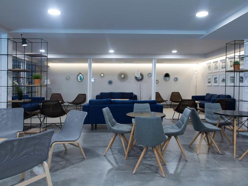 Espace lounge d'hôtel moderne avec chaises, tables et canapés dans une pièce lumineuse.