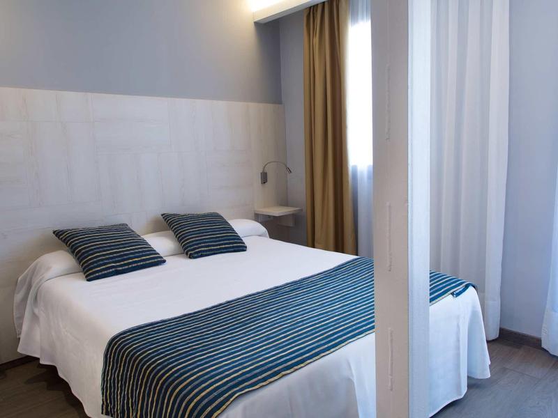 Chambre lumineuse avec un lit double et des oreillers et une couverture rayés bleus.