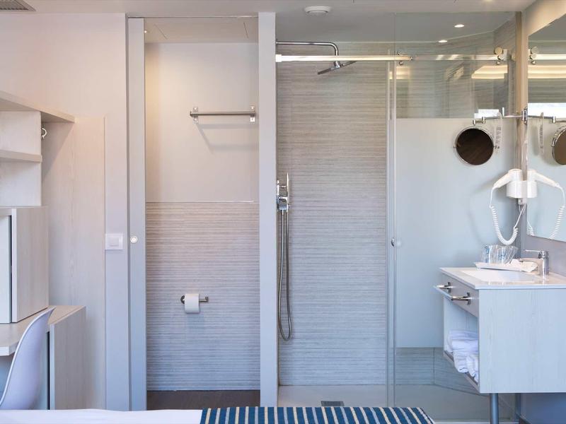 Salle de bain moderne avec douche, miroir, lavabo et bureau dans une chambre d'hôtel.
