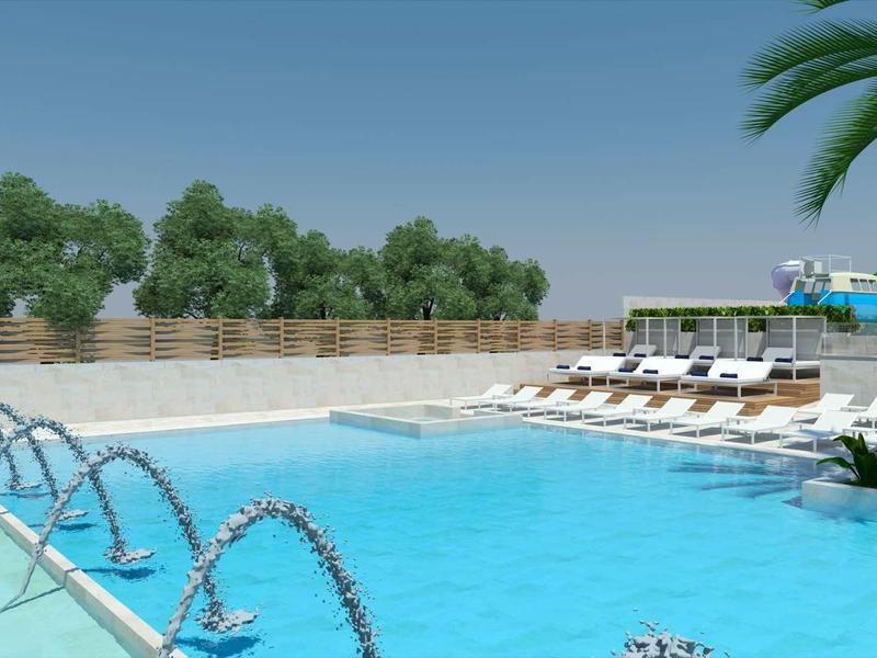 Piscina all'aperto con getti d'acqua, lettini e cielo azzurro.