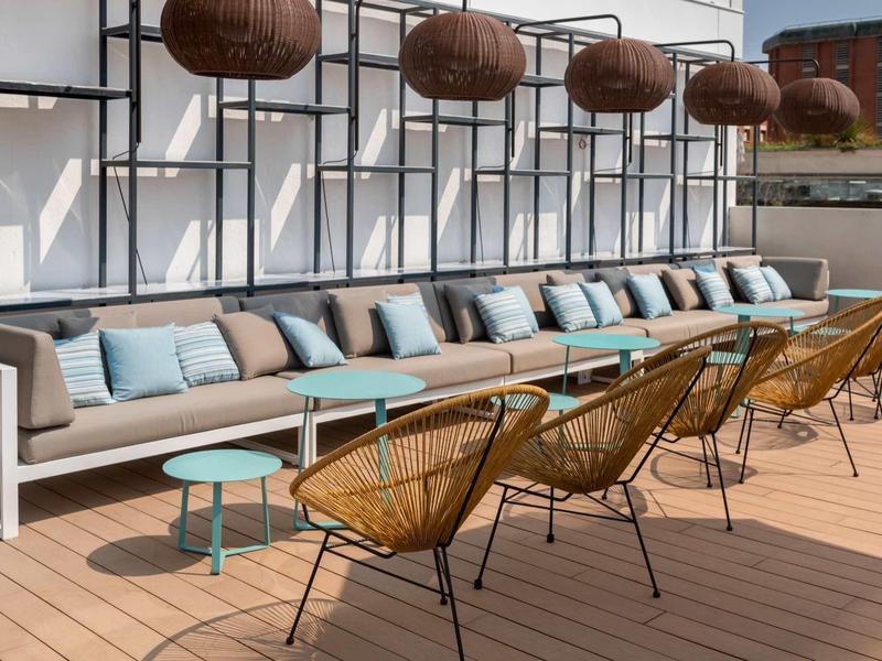 Area esterna moderna con divano, sedie e lampade appese su terrazza in legno.