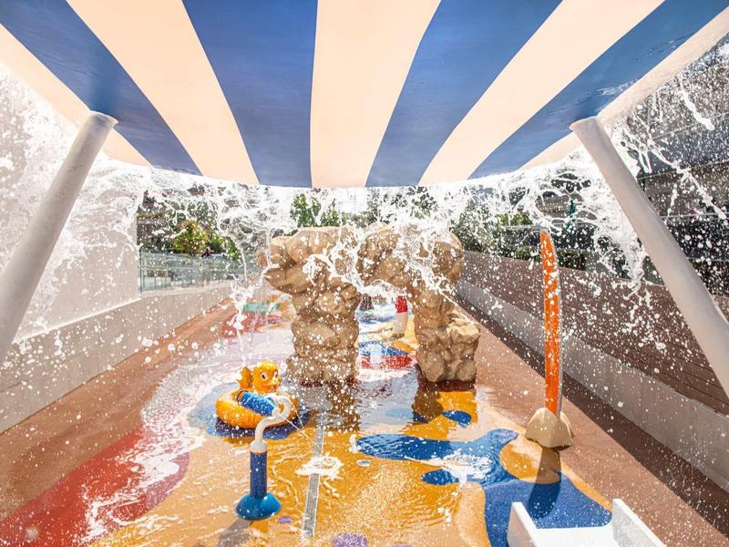 Parco acquatico con fontane colorate e tenda a righe blu e bianche.